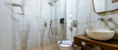 Un baño moderno con ducha de vidrio, pared de mármol, tocador de madera y un lavamanos grande.