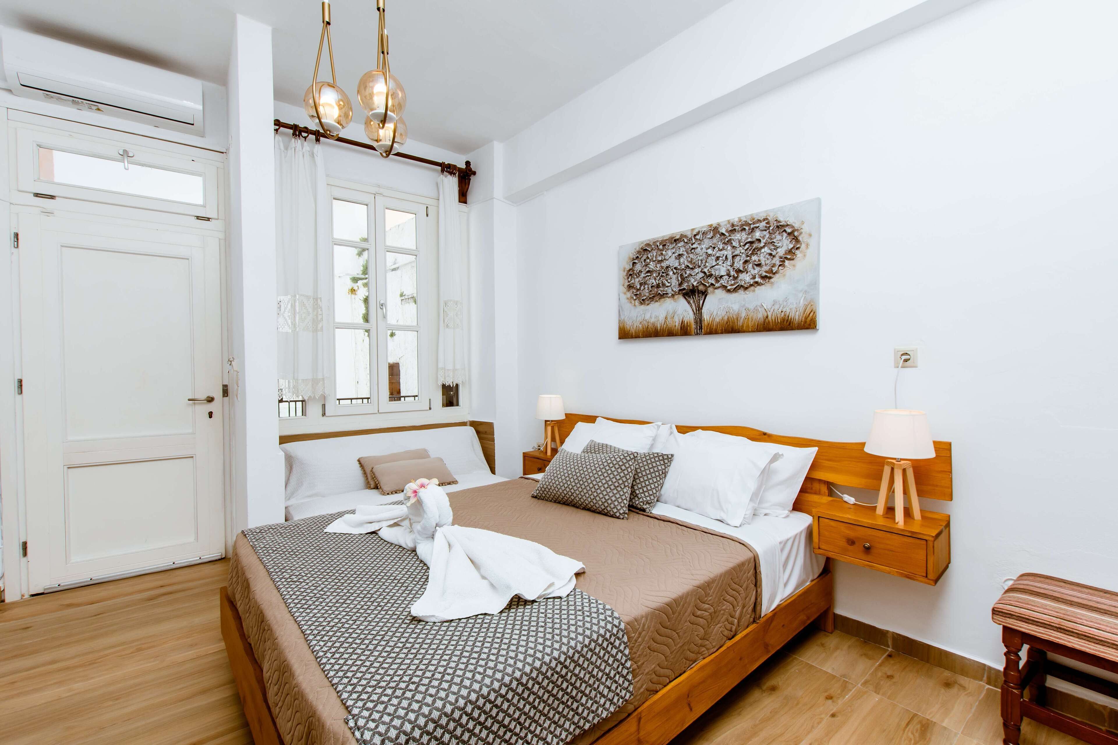 A neatly arranged bedroom with a large bed, bedside tables, a hanging light fixture, and a wall-mounted painting.