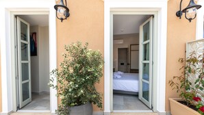 A hotel entrance with a large potted plant, a bed visible inside, and two open doors leading to the rooms. - El Greco (Chania)