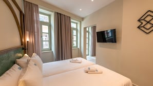 A hotel room with two beds, a flat-screen TV mounted on the wall, and a window with curtains. - El Greco (Chania)