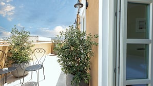 A rooftop terrace with outdoor seating, a potted plant, and a wall-mounted light fixture. - El Greco (Chania)
