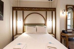 Habitación de hotel con una cama grande, dos almohadas, un cabecero de madera, una mesita de noche con un teléfono y un espejo.