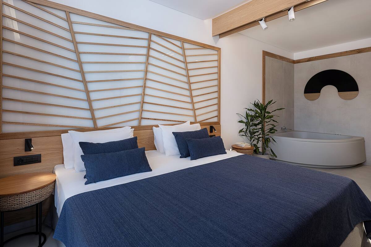 A modern bedroom with a large bed, a bedside table, a wall-mounted light, and a built-in bathtub.