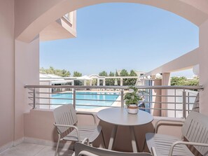 Un balcón con vista a la piscina, sillas blancas y una pequeña mesa con una planta.