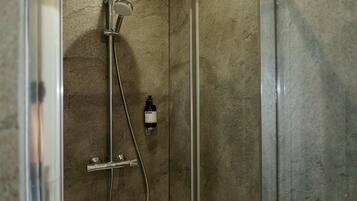 A shower with a handheld showerhead and a bottle of shampoo.