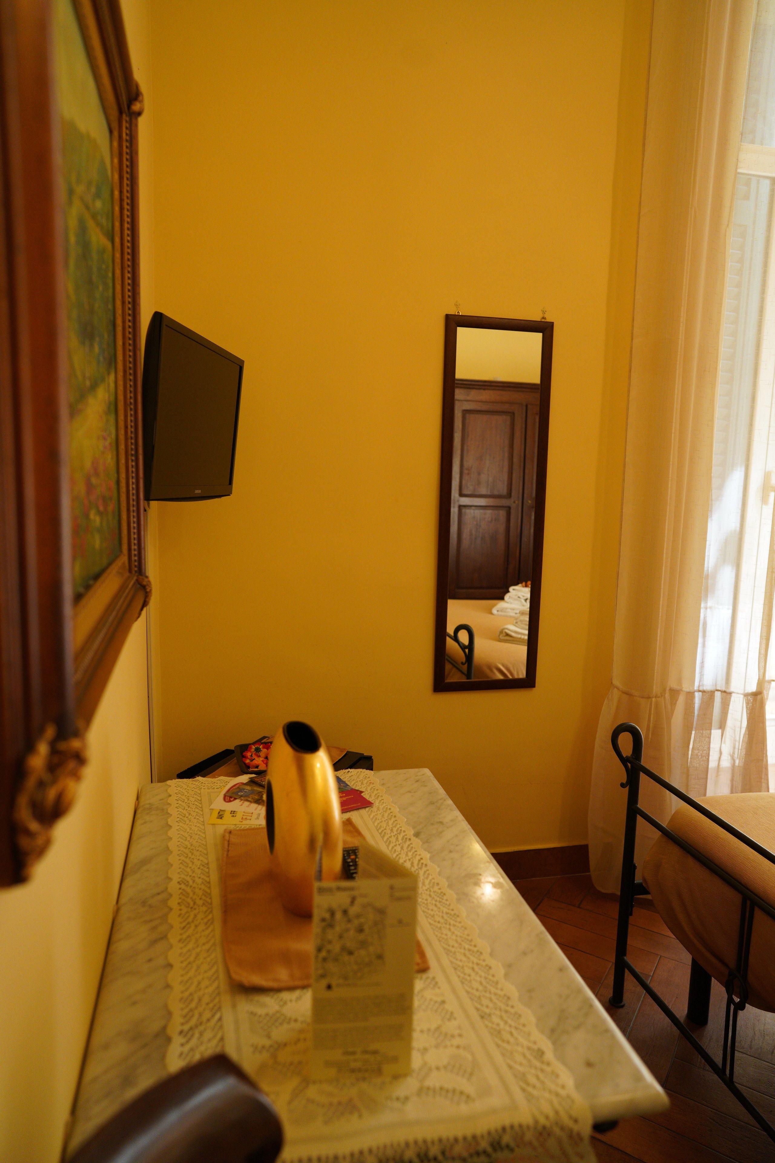 A hotel room with a bed, a bedside table, a mirror, and a window with curtains.
