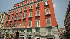 A multi-story building with a red facade, multiple balconies, and a ground-level entrance with a green awning. - Conte Cavour (Naples)