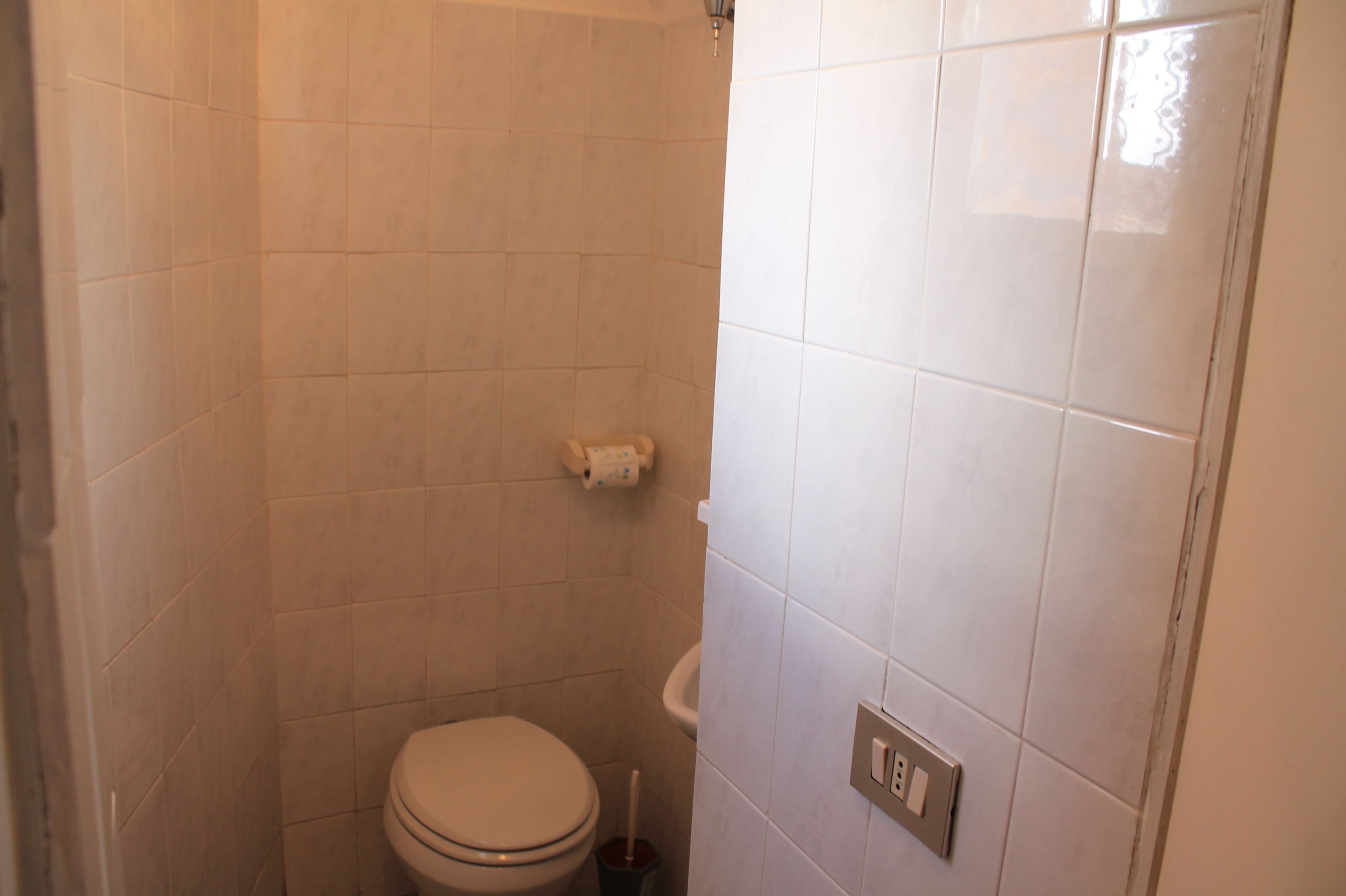 A small, tiled bathroom with a toilet, a sink, and a towel rack.