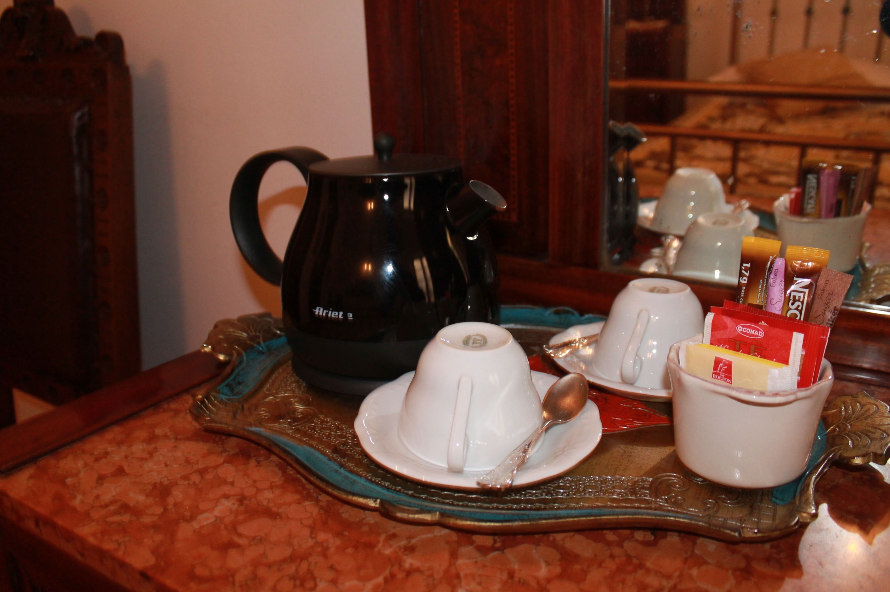 A coffee setup with a black coffee pot, two white cups, and a tray with a spoon and some packaged snacks.