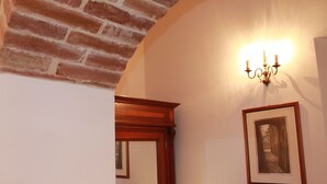 Un couloir avec un mur en briques, un cadre de porte en bois et un luminaire fixé au mur.