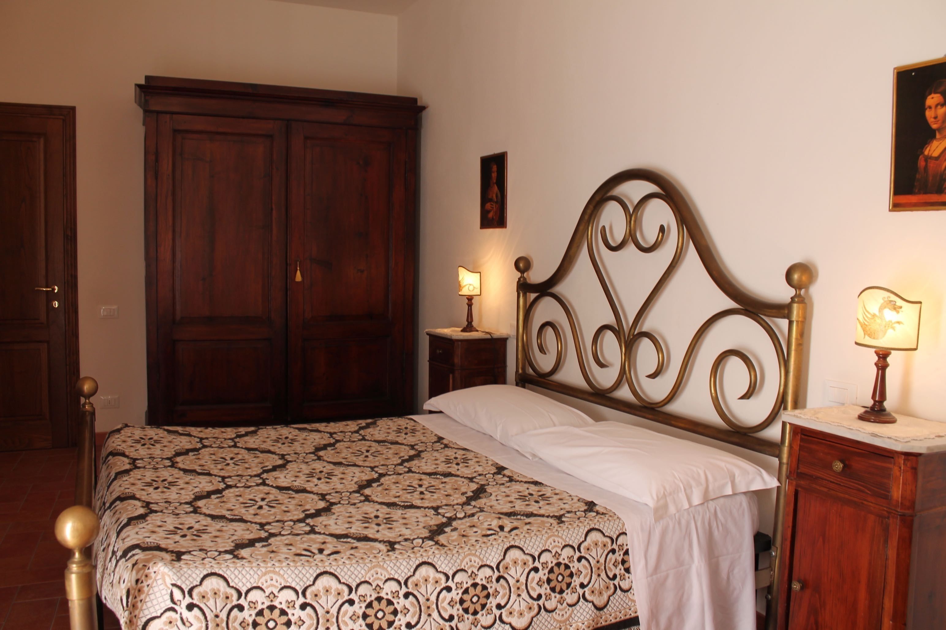 Un dormitorio con una cama grande, un armario de madera, mesitas de noche con lámparas y un cuadro en la pared.