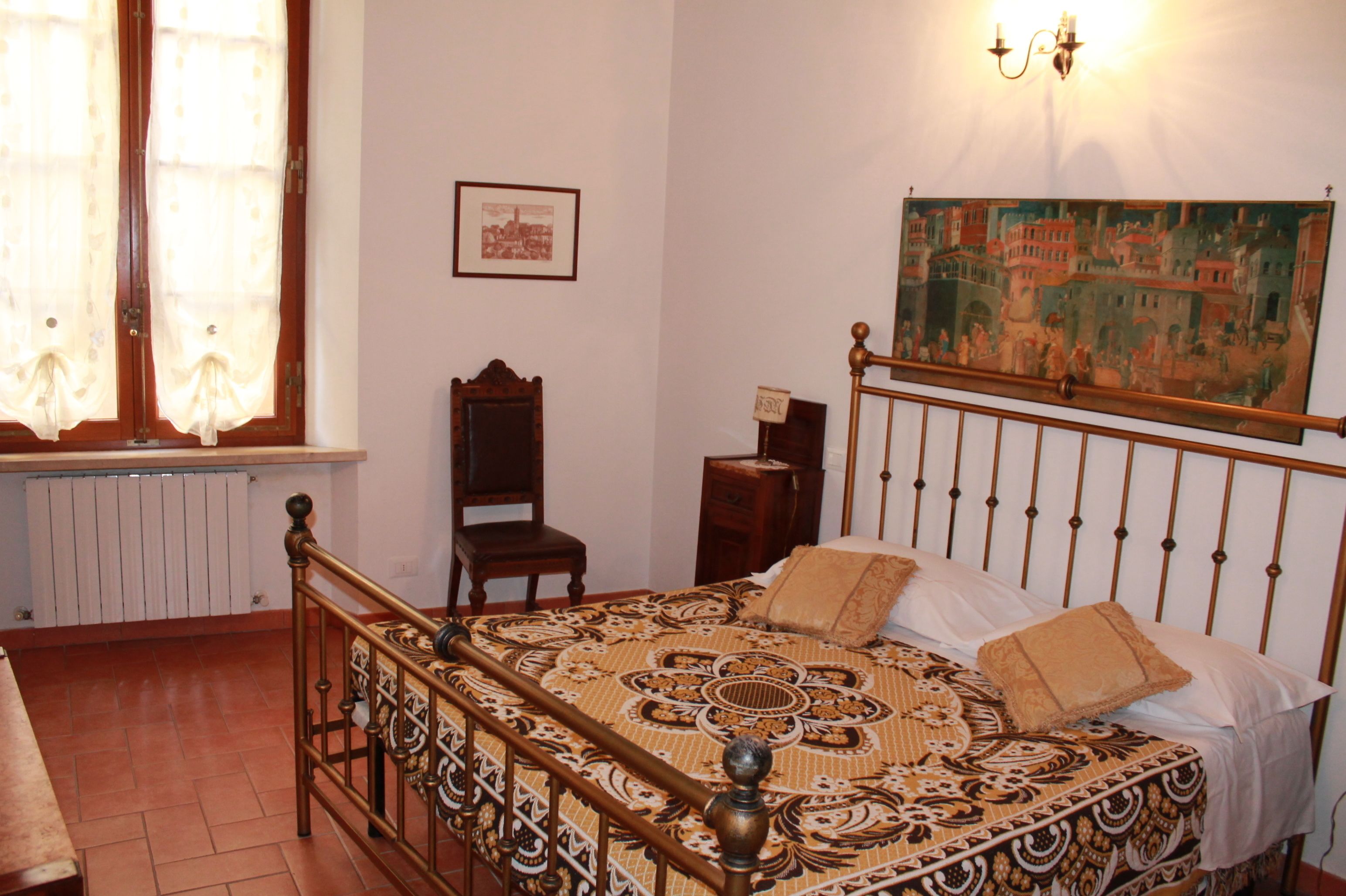 A bedroom with a bed, a chair, a radiator, a painting on the wall, and a window with curtains.