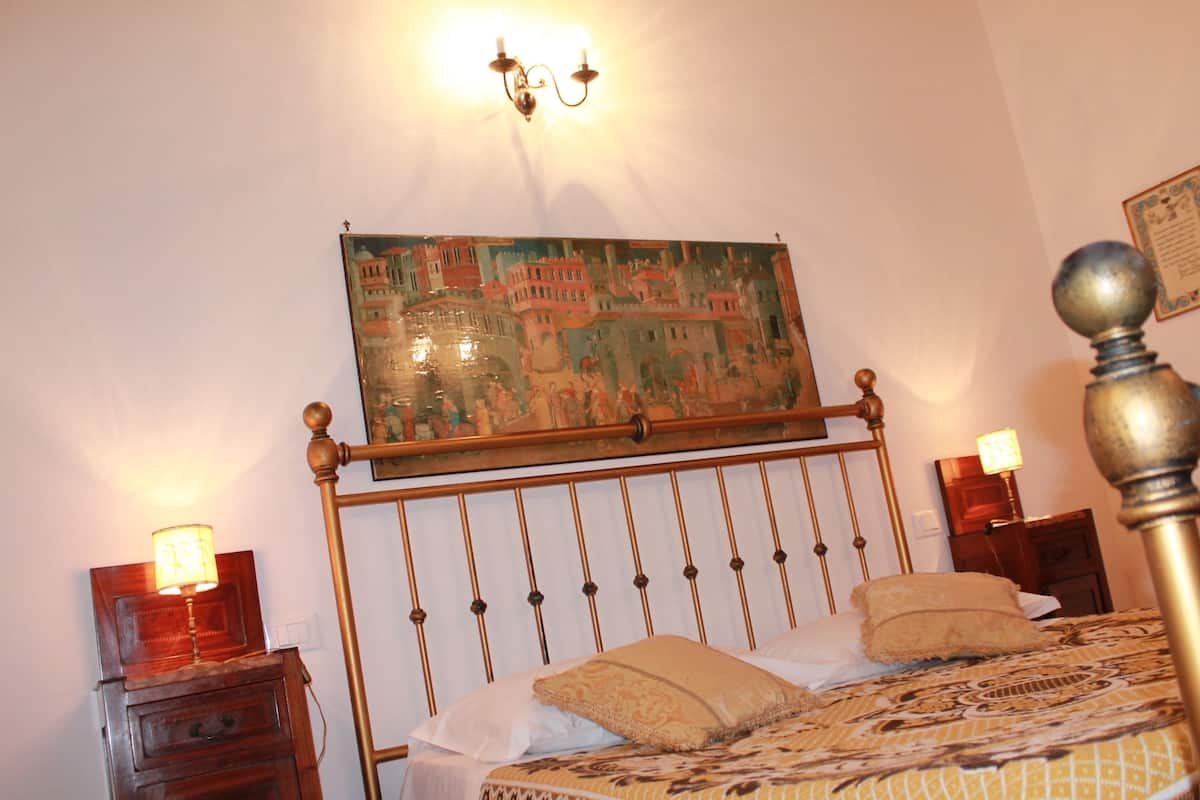 A bedroom with a bed, a nightstand, a wall-mounted lamp, and a painting.
