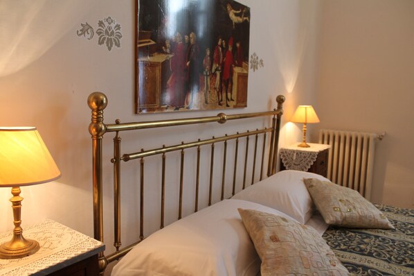 A bedroom with a bed, two bedside lamps, a radiator, and a wall-mounted painting.