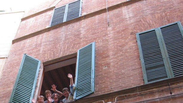 Un immeuble à plusieurs étages avec des volets verts aux fenêtres et des balcons.