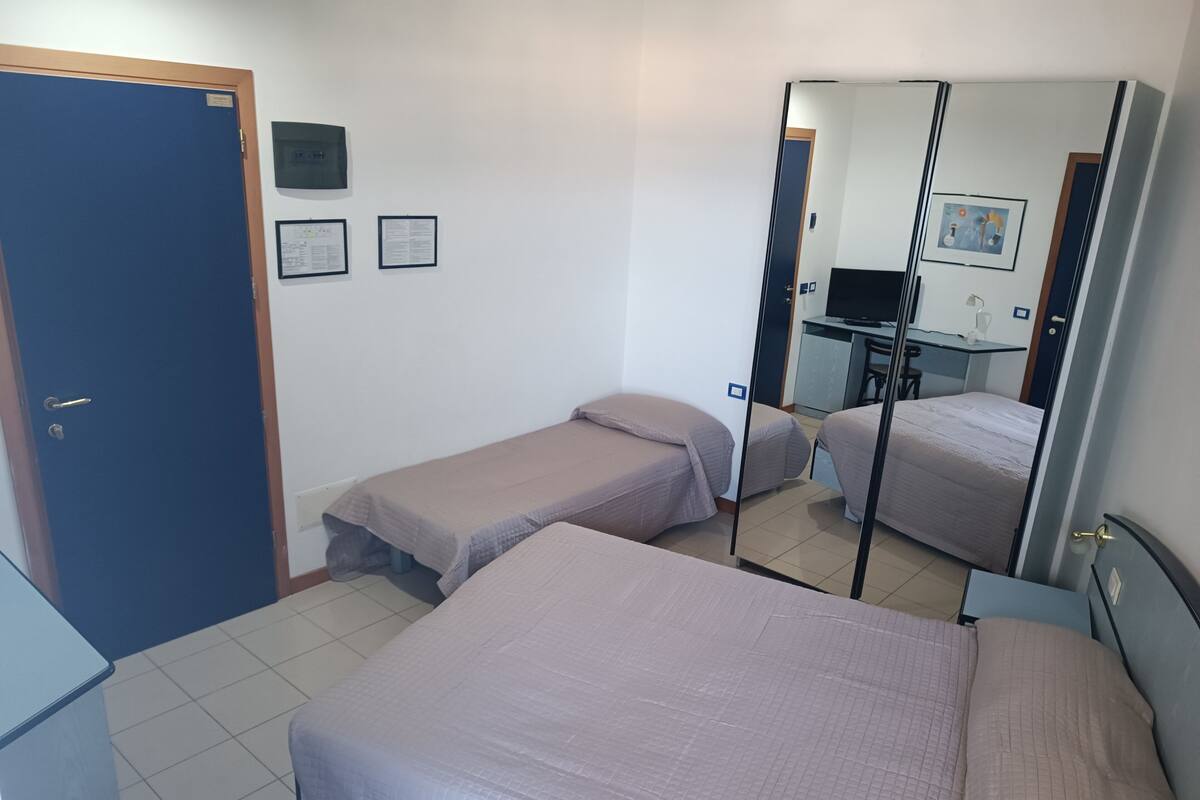 A room with two single beds, a desk with a chair, a mirror, and a door.
