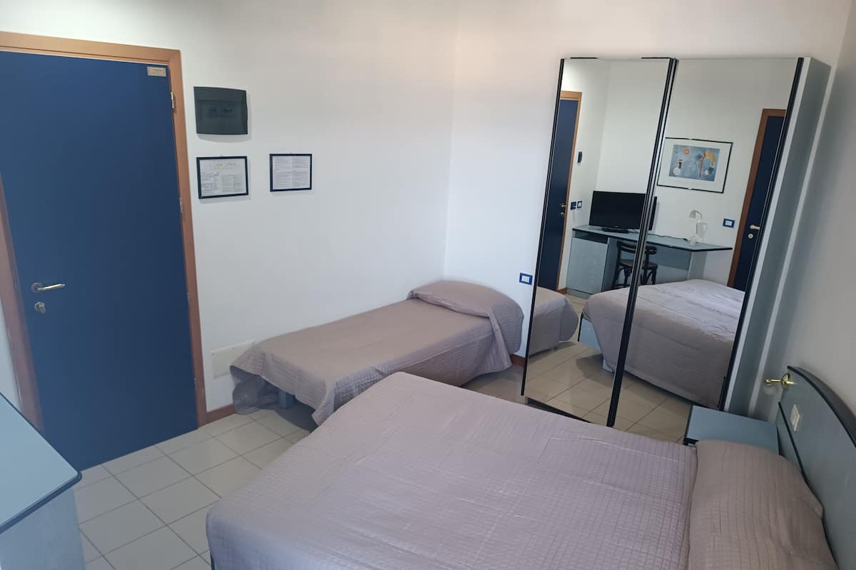 A room with two single beds, a desk with a chair, a mirror, and a door.