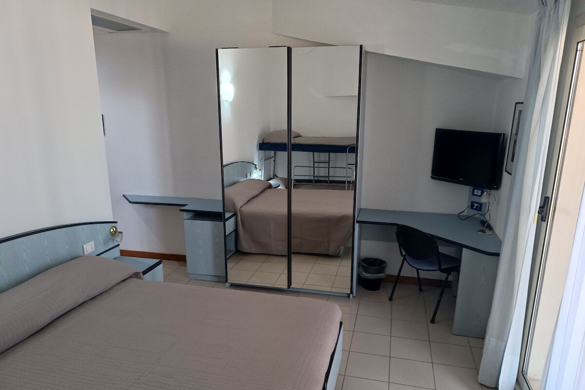 A hotel room with two beds, a desk, a chair, a television, and a wardrobe.