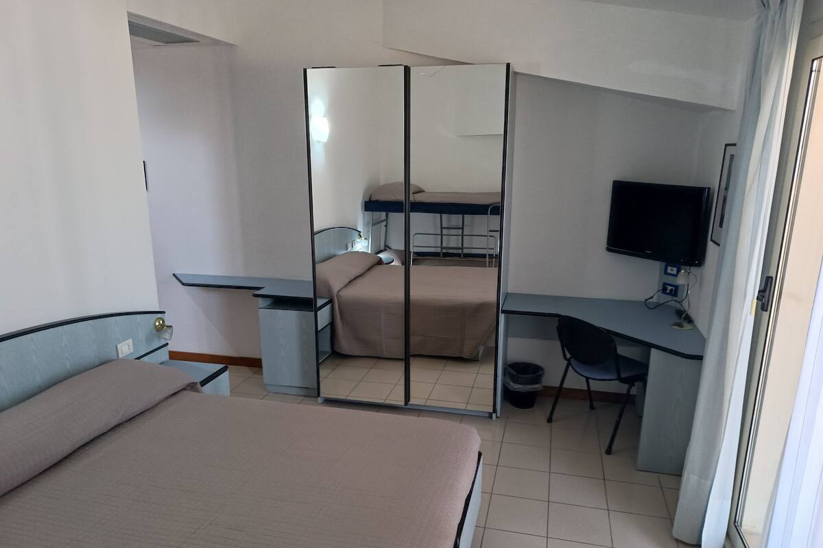 A hotel room with two beds, a desk, a chair, a television, and a wardrobe.