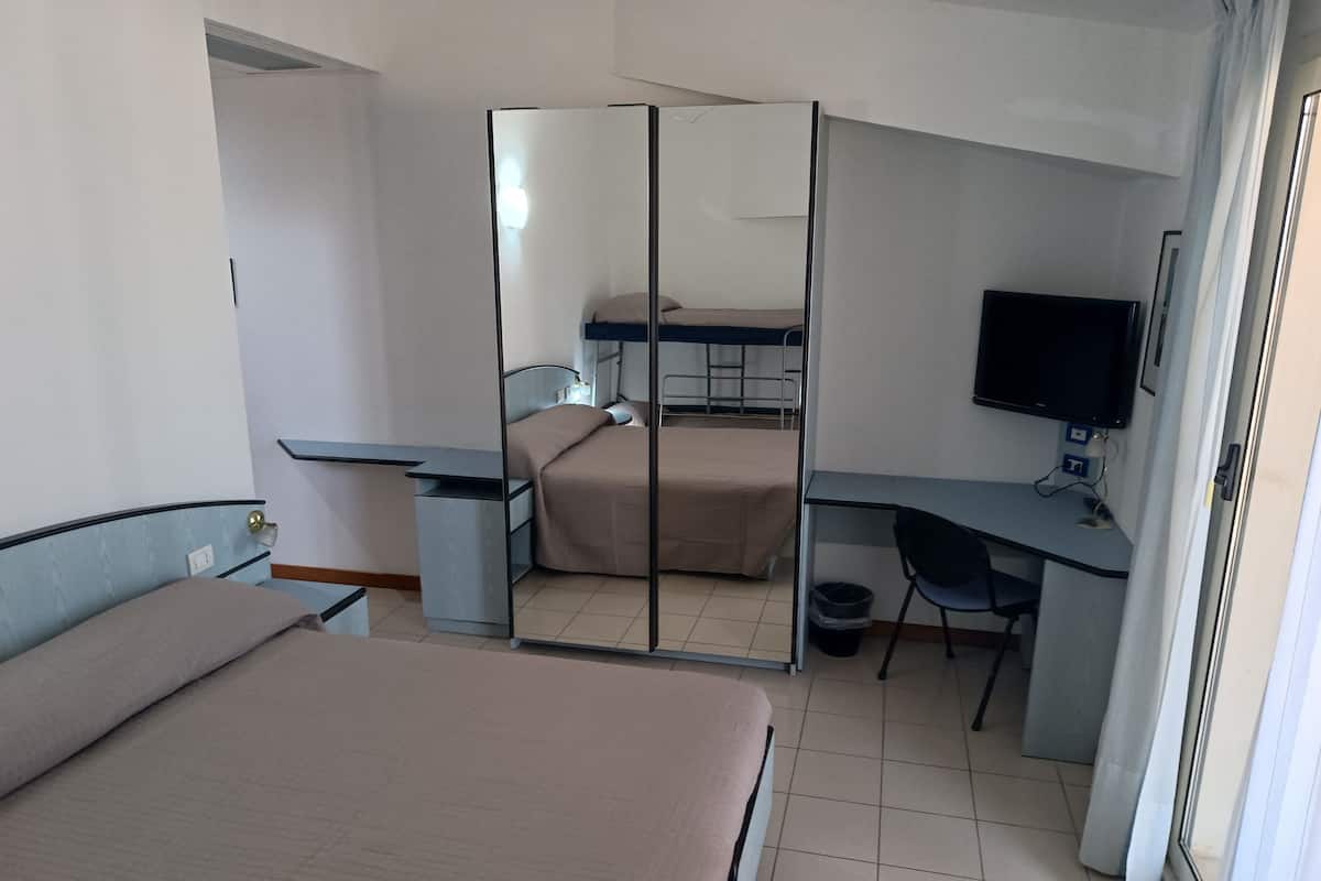 A hotel room with a bed, a desk, a chair, a television, and a mirror.
