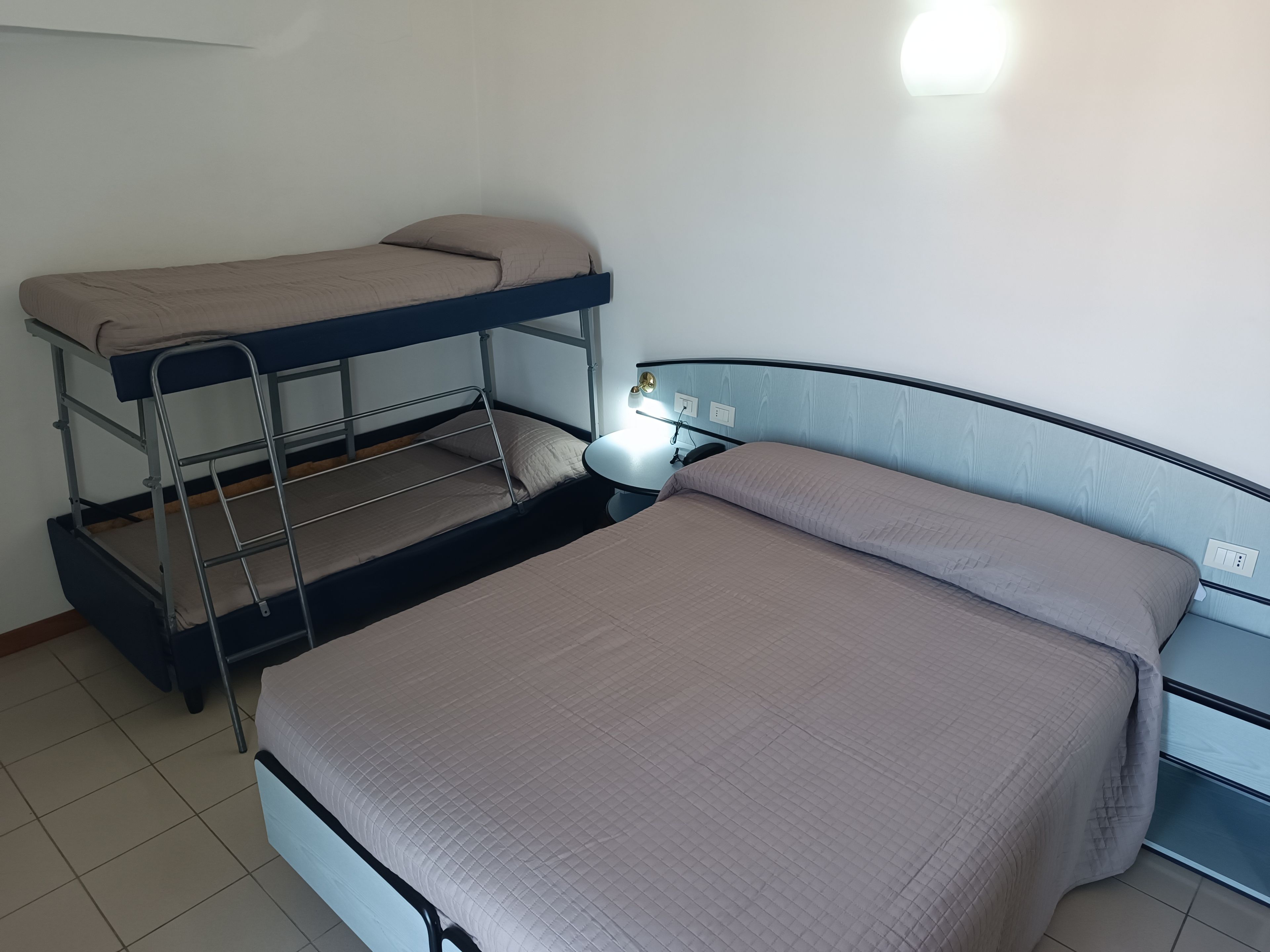 A bunk bed room with a single bed and a desk with a lamp.