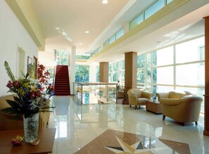 A spacious lobby with a staircase, a glass railing, and a seating area with a sofa and armchairs. - Remin Plaza (Rimini)