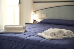 A neatly made bed with a blue quilt and white towels. - Remin Plaza (Rimini)