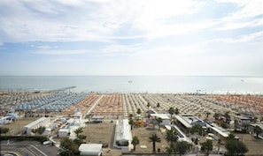 Ein Strand mit vielen Sonnenschirmen und Liegestühlen, einer Seebrücke, die ins Meer führt, und einem klaren Himmel.