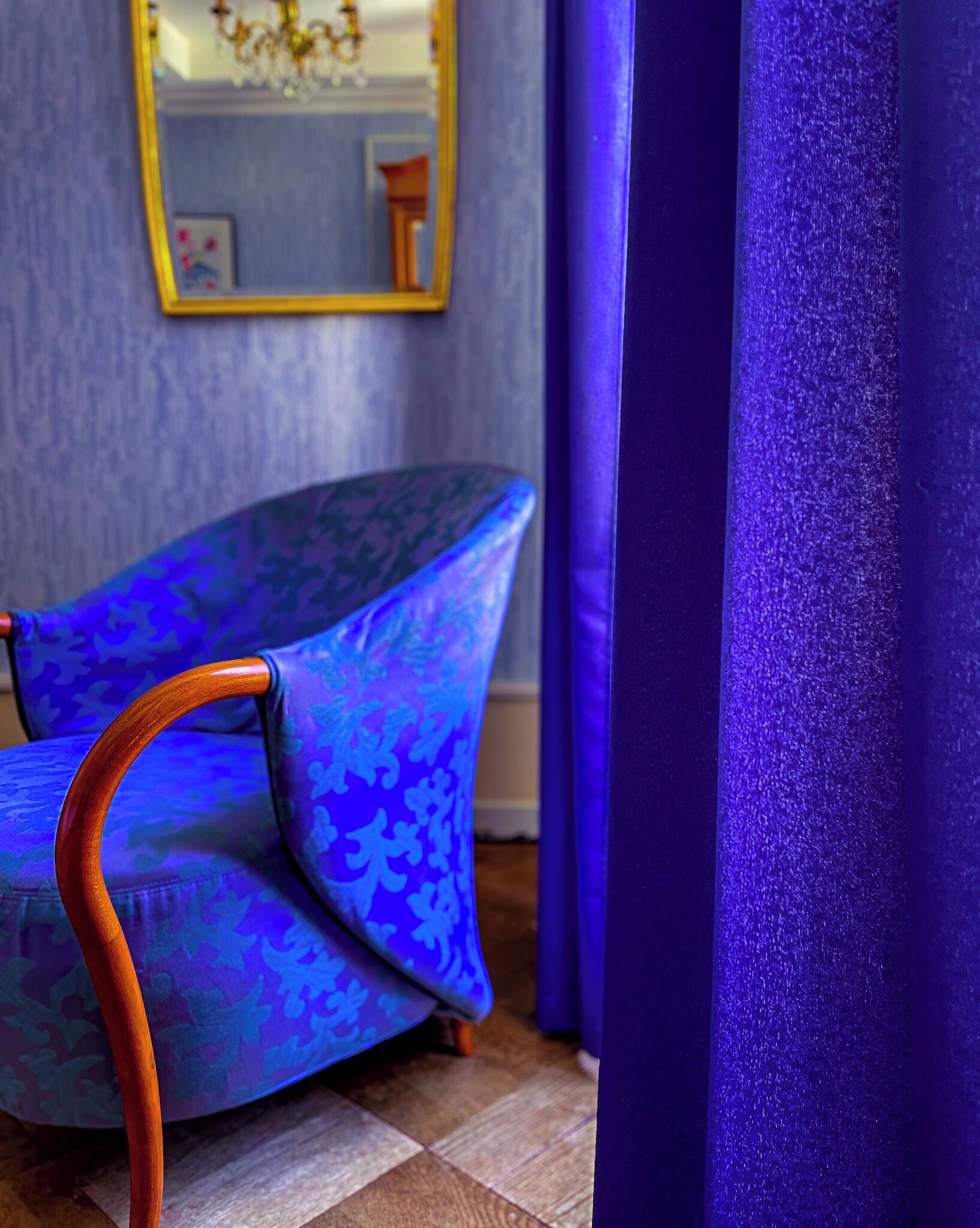 A room with a patterned chair, a mirror, and a curtain.