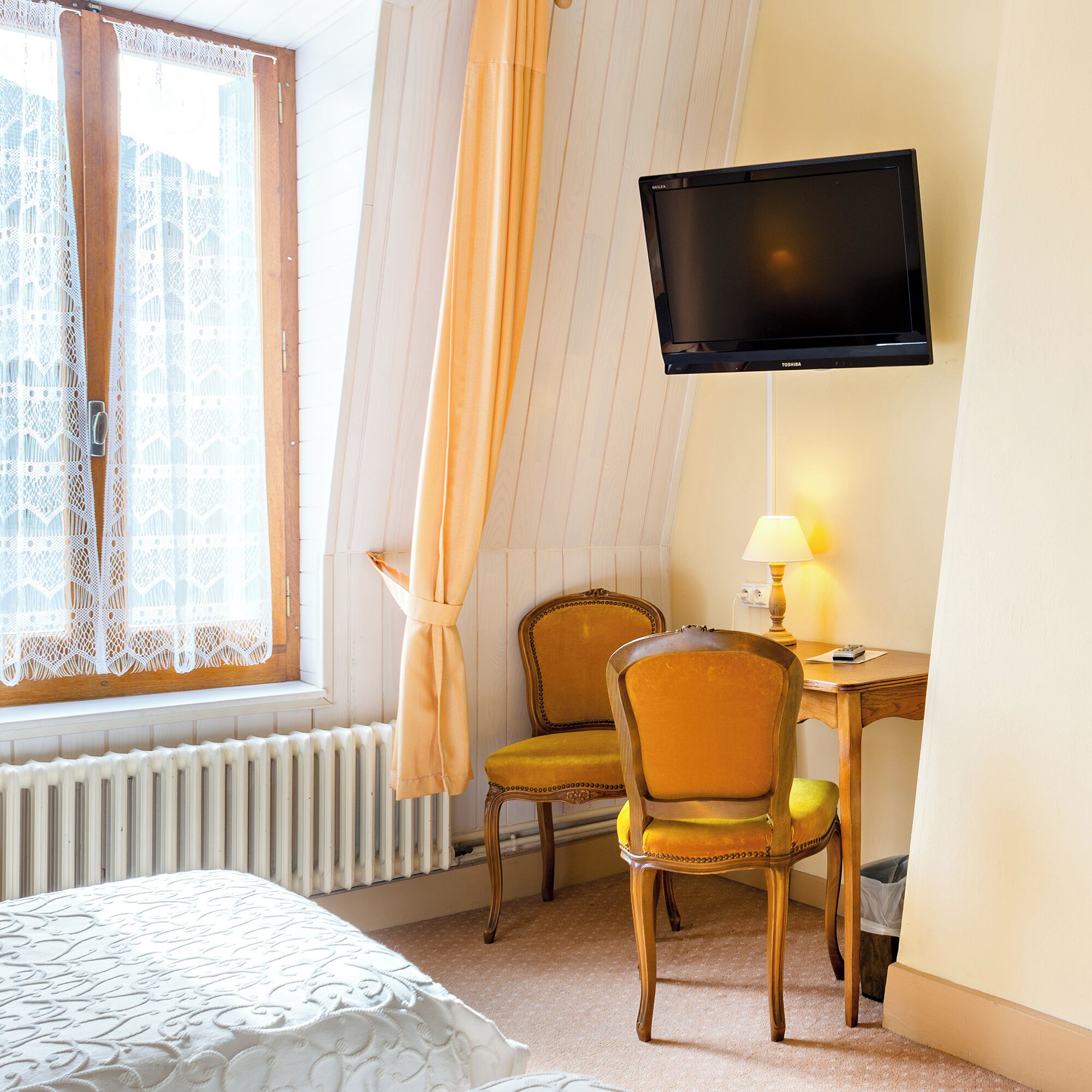Habitación de hotel con cama, dos sillas, escritorio, televisor y ventana con cortinas.