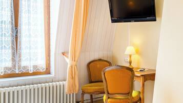 Habitación de hotel con cama, dos sillas, escritorio, televisor y ventana con cortinas.