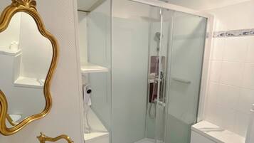 A bathroom with a white sink, a gold ornate mirror, a glass-enclosed shower, and a white toilet.