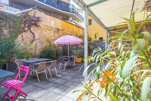 Un espace extérieur aménagé en terrasse, avec des tables et des chaises, un parasol rose et des plantes en pot.