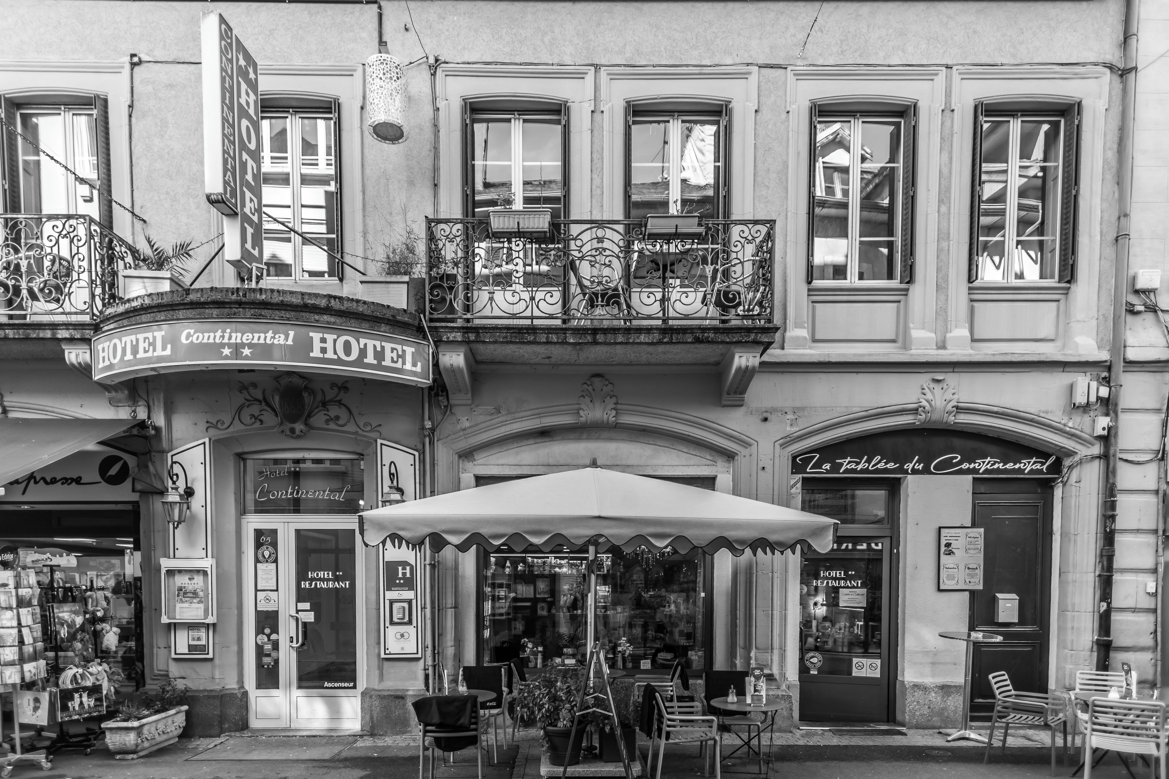 A black and white view of a hotel with a balcony, outdoor seating, and a restaurant.