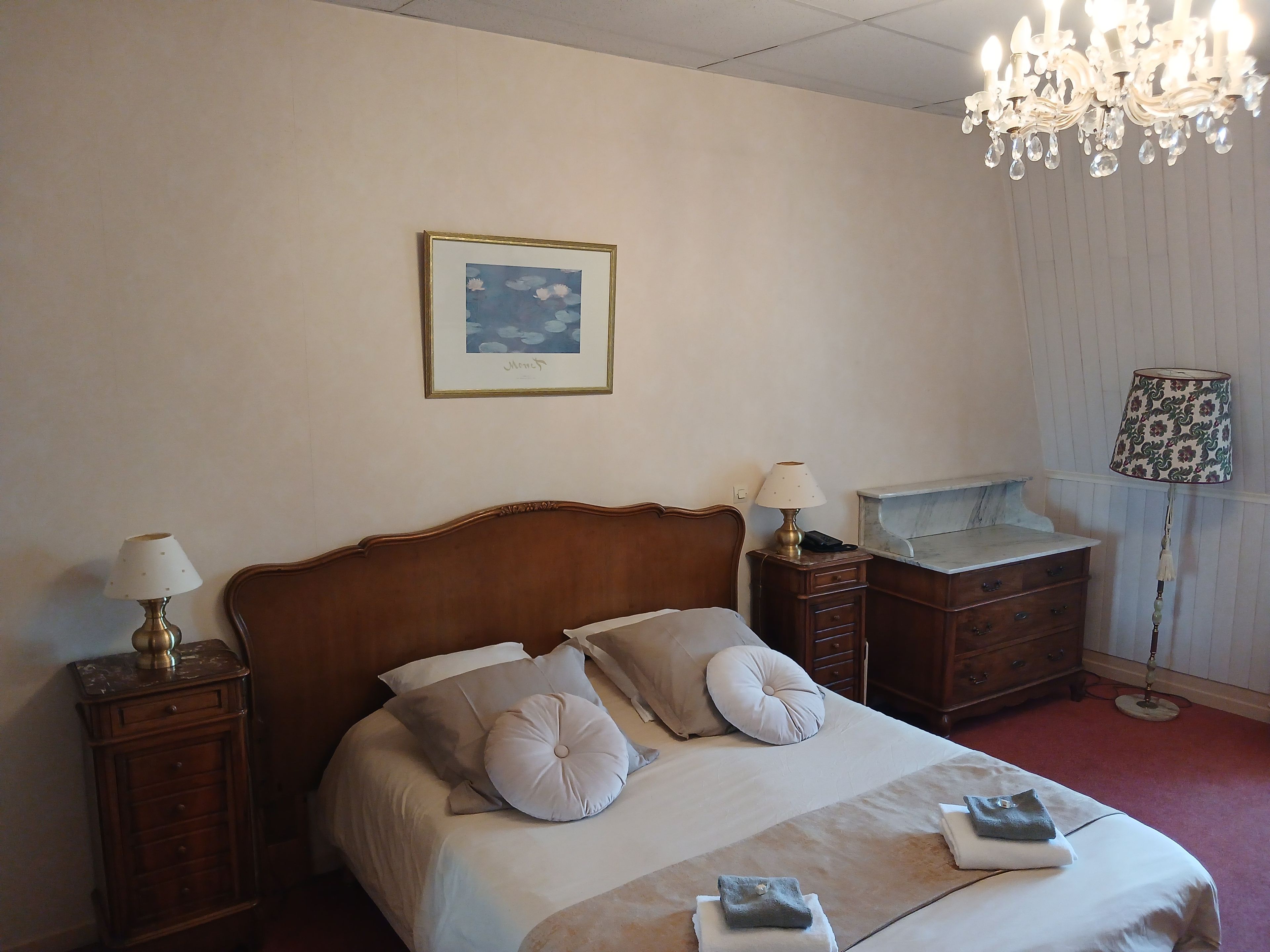 Habitación de hotel con cama, dos mesitas de noche, una araña, un cuadro enmarcado en la pared y un aparador.