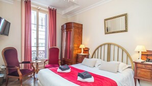 Une chambre d’hôtel comprenant un lit, deux chaises, une armoire en bois, un bureau, une lampe et un téléviseur.