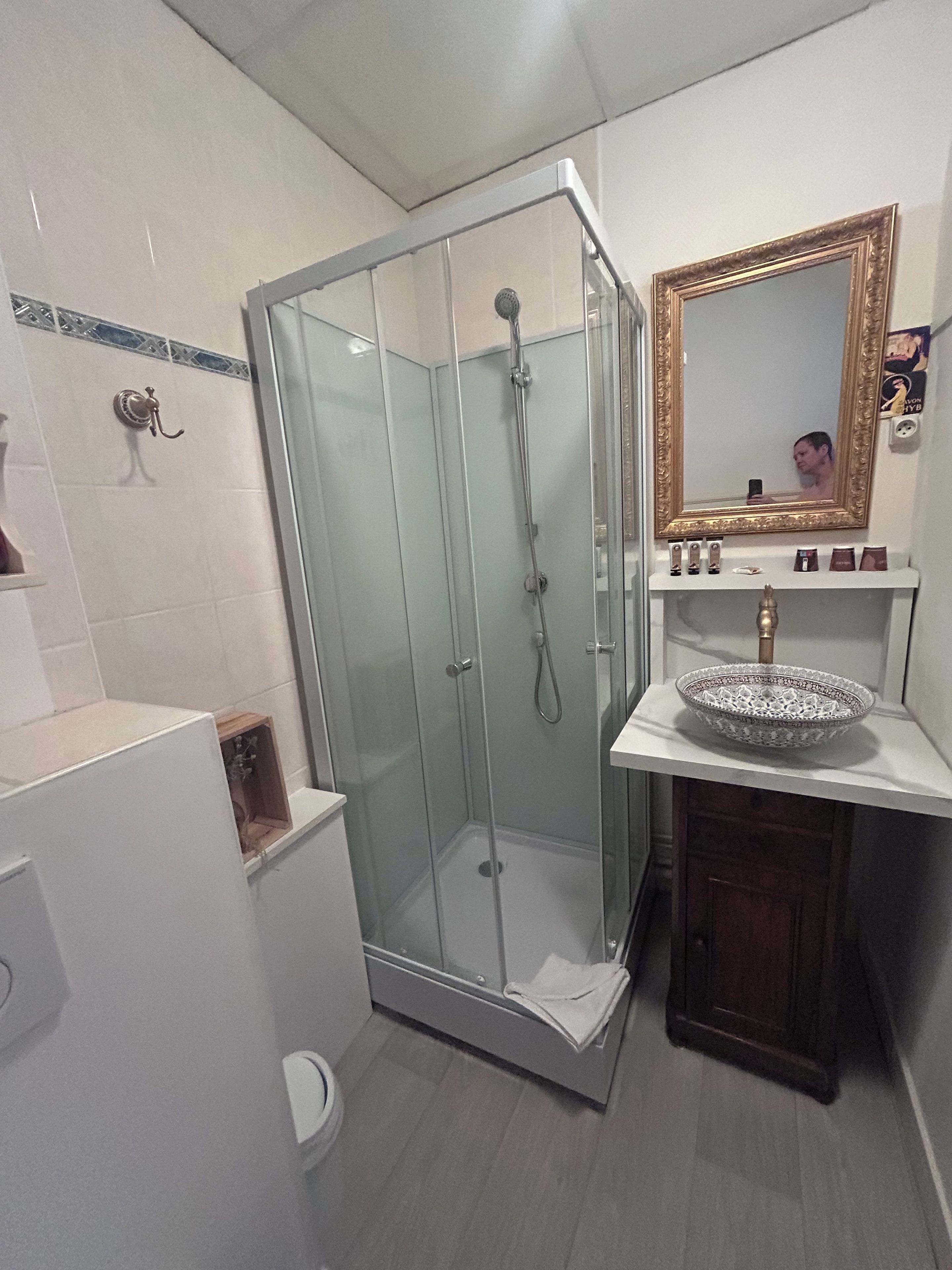 A bathroom with a glass-enclosed shower, a sink with a decorative bowl, and a mirror with a gold frame.