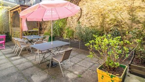 Une terrasse extérieure avec des tables et des chaises, un parasol rose et une plante en pot.