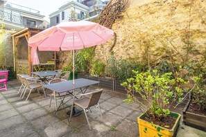 An outdoor patio with tables and chairs, a pink umbrella, and a potted plant. - Hotel Continental (Evian-les-Bains)