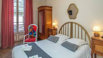 A hotel room with a bed, a chair, a wardrobe, a mirror, and a window with curtains.