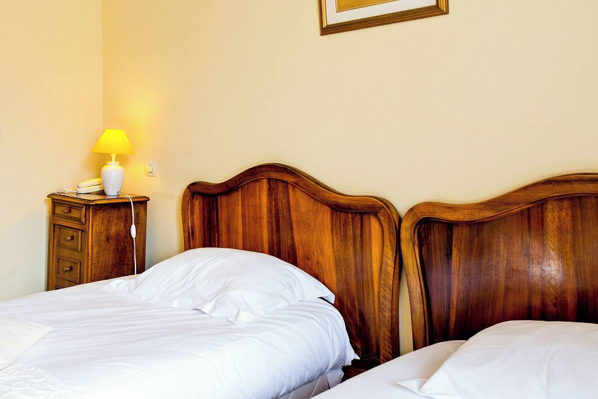 Hotellihuone, jossa on kaksi sänkyä, yöpöytä lampun kanssa ja taulu seinällä.