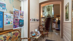 Un espace d'accueil comprenant un escalier, un comptoir de réception et un espace d'attente avec des meubles à motifs floraux.