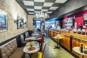 L’intérieur d’un restaurant avec des banquettes, des tables, un bar et un lustre.