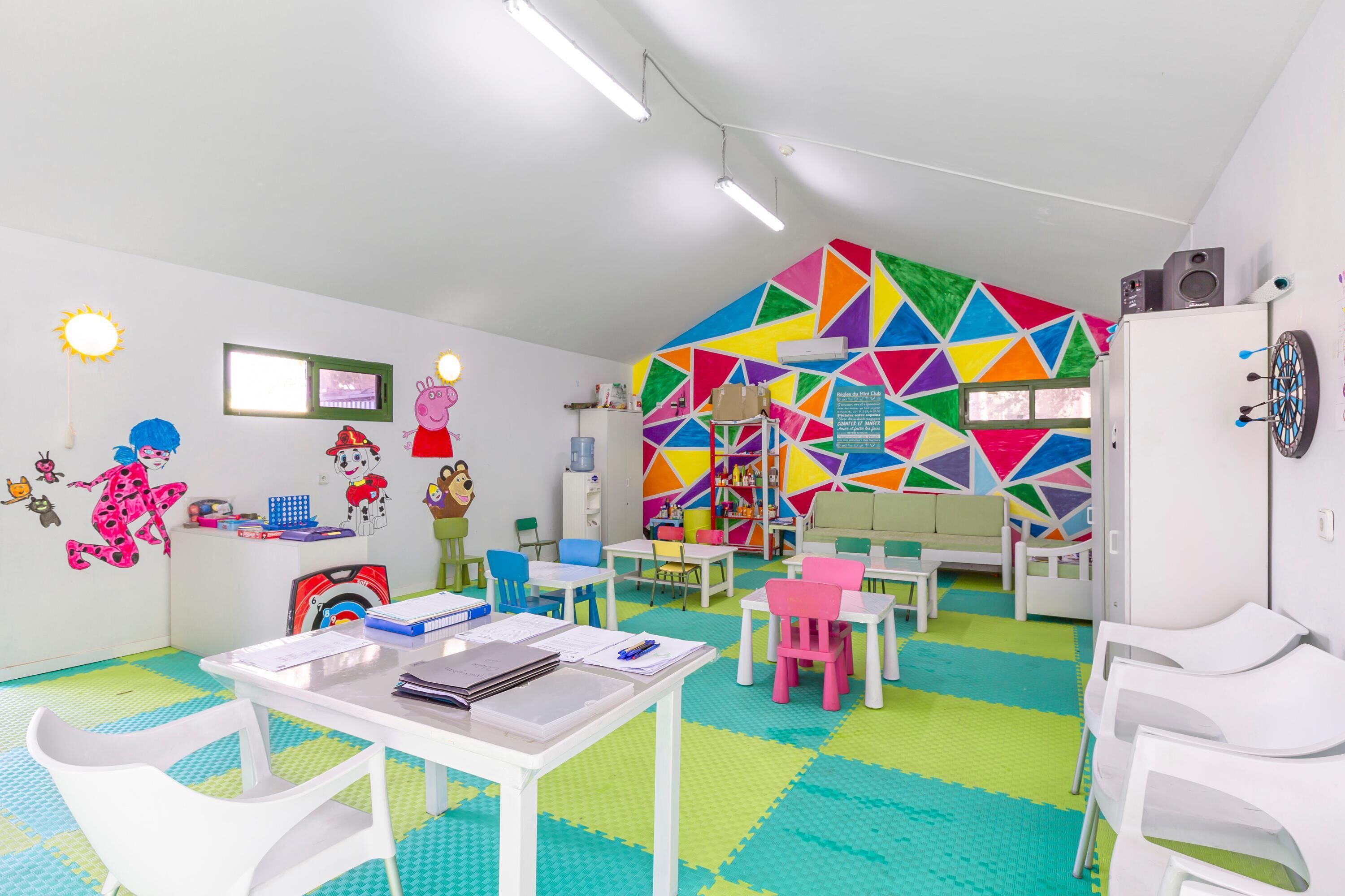 Ein helles Kinderzimmer mit farbenfrohem Wanddesign, weißen Möbeln und lehrreichen Spielzeugen.