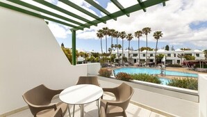 A balcony with a table and chairs, a pool, and palm trees in the background. - Hotel THB Royal (Yaiza)