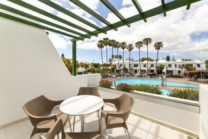 A balcony with a table and chairs, a pool, and palm trees in the background. - Hotel THB Royal (Yaiza)