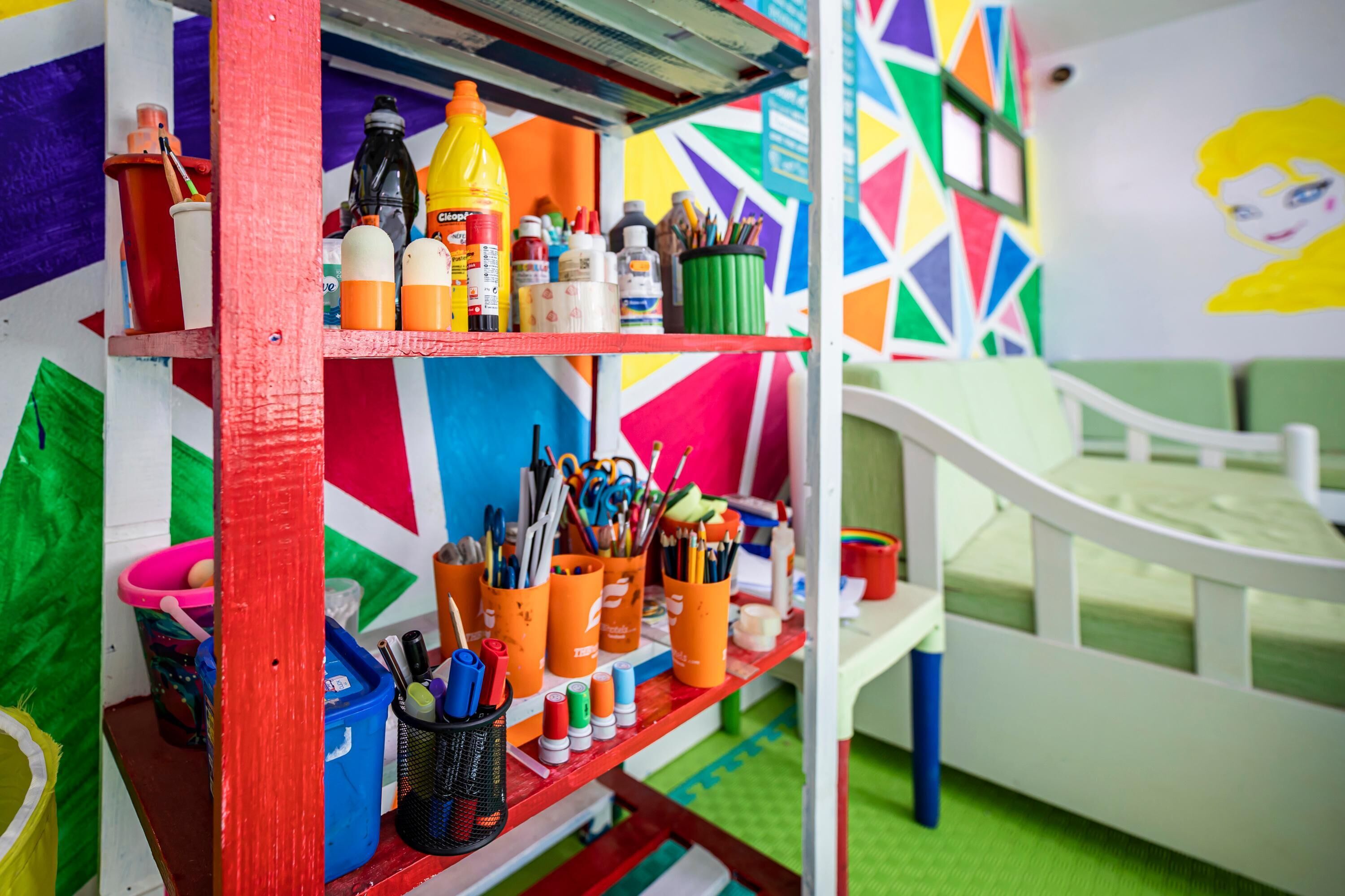 A colorful room with a bed, a shelf with art supplies, and a wall with a geometric pattern.