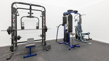 Un gimnasio con una estructura para sentadillas, banco de pesas y varias máquinas de ejercicio con pesas.