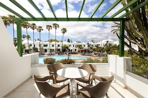 A covered outdoor area with a pool, palm trees, and a view of a resort. - Hotel THB Royal (Yaiza)