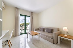 A modern living room with a sofa, two side tables, a lamp, a chair, and a view through a door. - Hotel THB Royal (Yaiza)